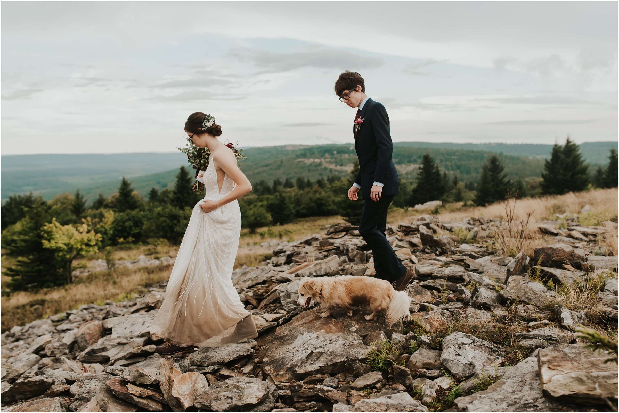 bride and groom with dog, walking on rocks on top of a mountain